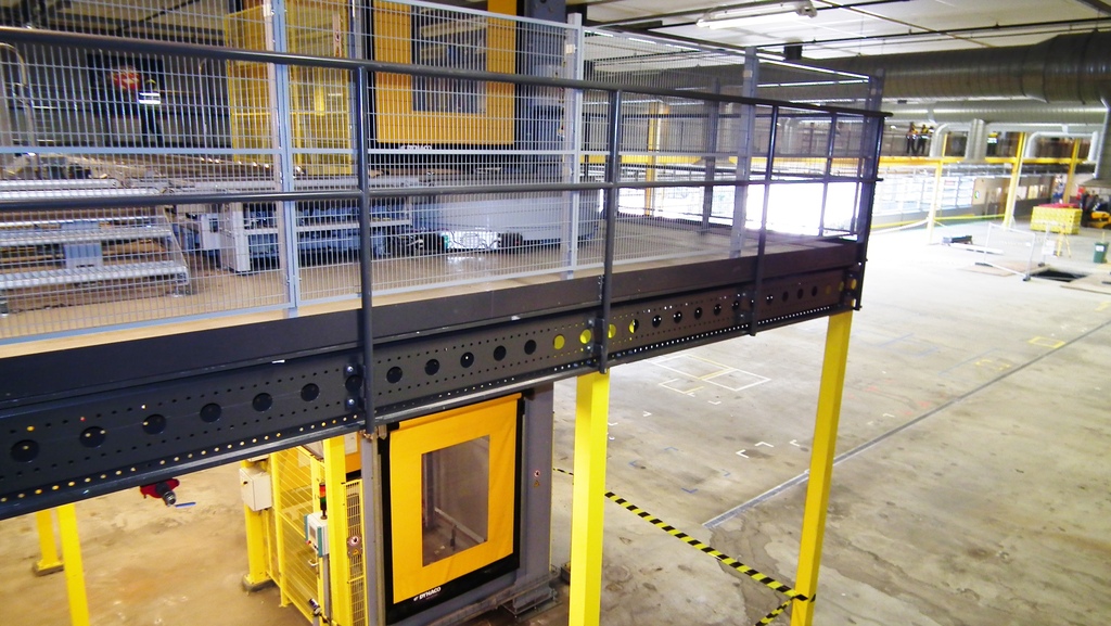 Teollisuushallin välitasorakenne nostimella ja suojaverkoilla turvalliseen varastointiin.
